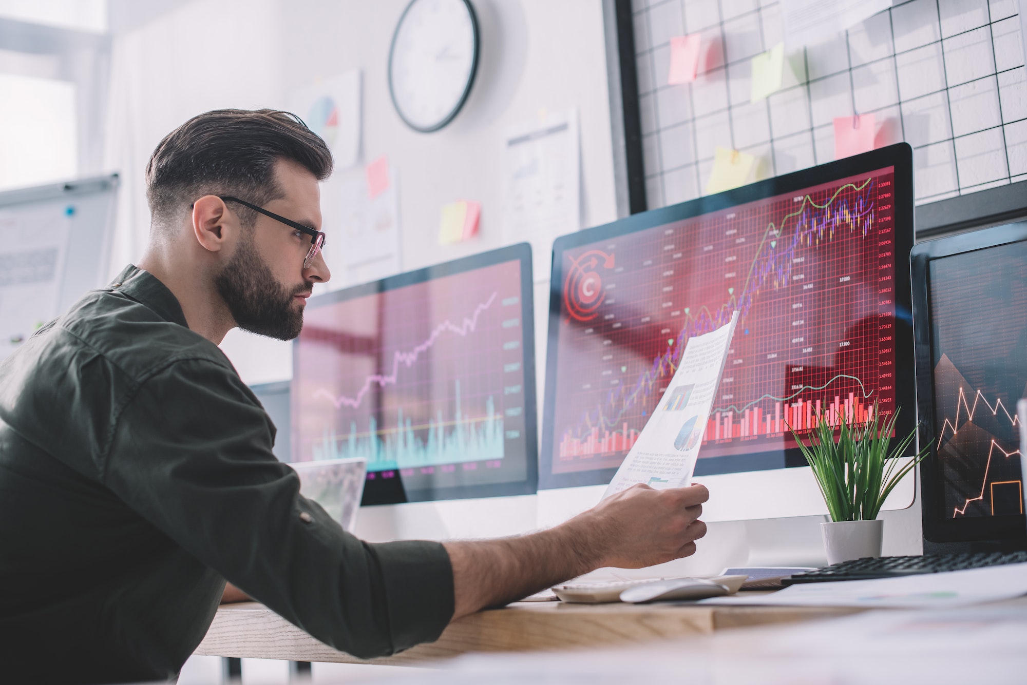 Side view of information security analyst looking at charts near graphs on computer monitors in